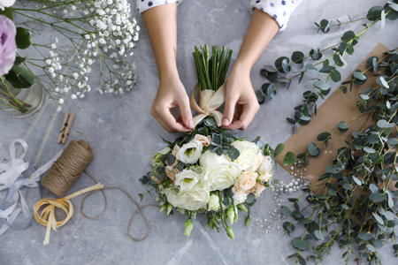 Florist tieing bow on beautiful wedding bouquet at light gray marble table, top viewの写真素材