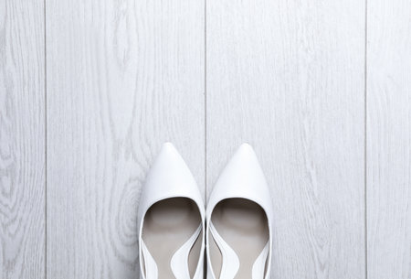 Pair of wedding high heel shoes on white wooden floor, flat lay. Space for textの写真素材