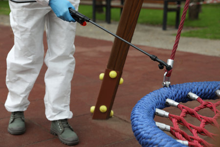 Woman wearing chemical protective suit with disinfectant sprayer on playground, closeup. Preventive measure during coronavirus pandemicの写真素材