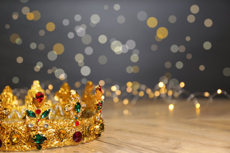 Beautiful golden crown with gems and fairy lights on wooden table, space for text. fantasy itemの写真素材