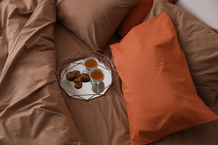 Cups of hot drink and cookies on bed with brown lines in stylish room, above viewの写真素材