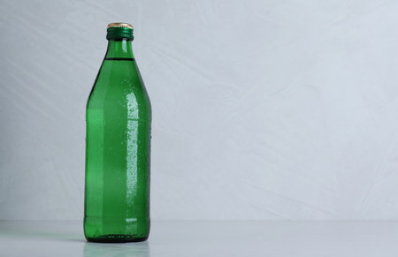 Glass bottle with water on light gray background, space for textの写真素材