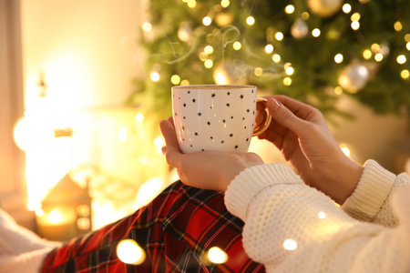 Woman with cup of hot drink near Christmas tree indoors, closeupの写真素材