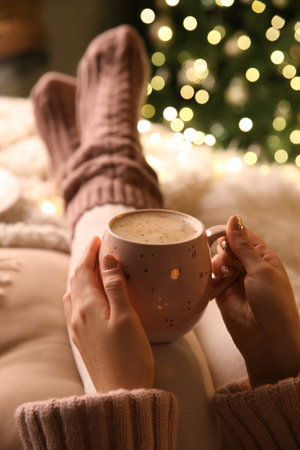 Woman holding cup of delicious hot drink near Christmas tree indoors, closeupの写真素材