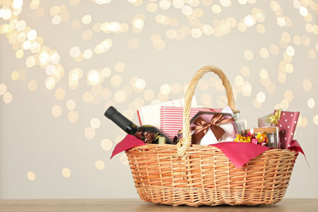 Wicker basket with gifts, wine and food against blurred festive lights. Space for textの写真素材