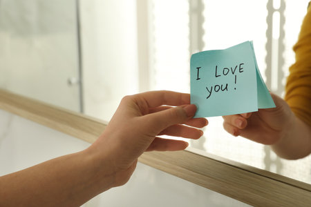 Woman putting sticky note with text I love you! on mirror, close upの写真素材