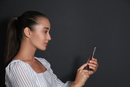 Young woman unlocking smartphone with facial scanner on black background. biometric verification