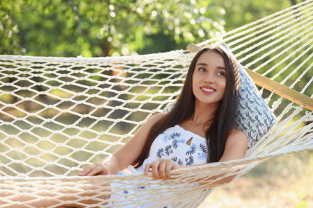 Young woman resting in comfortable hammock at green gardenの写真素材
