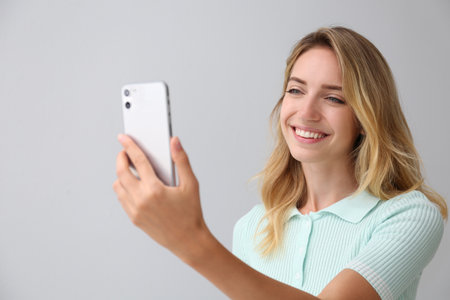 Young woman unlocking smartphone with facial scanner on gray background. biometric verificationの写真素材