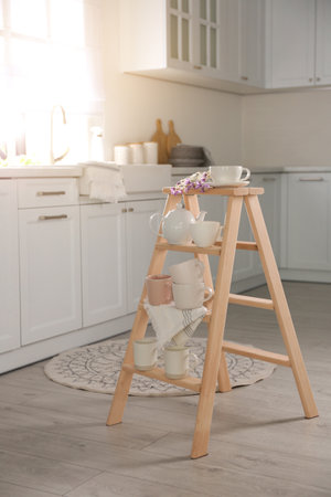 Decorative ladder with different dishware and field flowers bouquet in stylish kitchen. Idea for interior designの写真素材