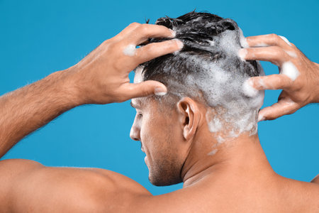 Handsome man washing hair on light blue background, back viewの写真素材