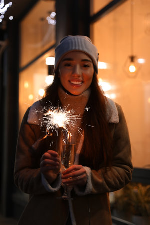 Happy young woman with sparkler and glass of champagne at winter fairの写真素材