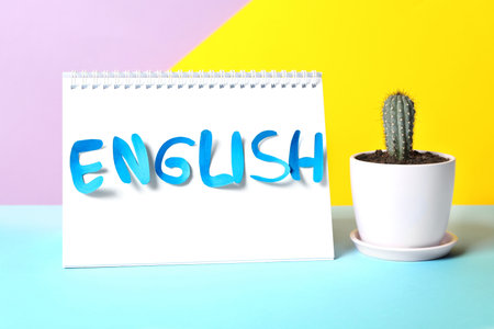 Notepad with word English and cactus on light blue tableの写真素材