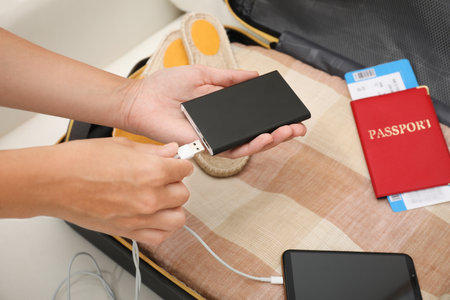 Woman charging smartphone with power bank near packed suitcase indoors, closeupの写真素材