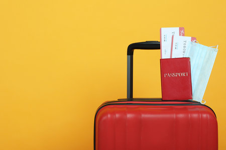 Passport with tickets and protective mask on suitcase against yellow background, space for text. Travel during quarantineの写真素材