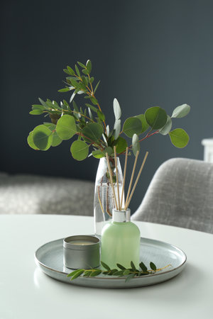 Eucalyptus branches, candle and aromatic reed air freshener on white table indoors. interior...