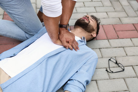 Passerby performing CPR on unconscious young man outdoors. First aidの写真素材