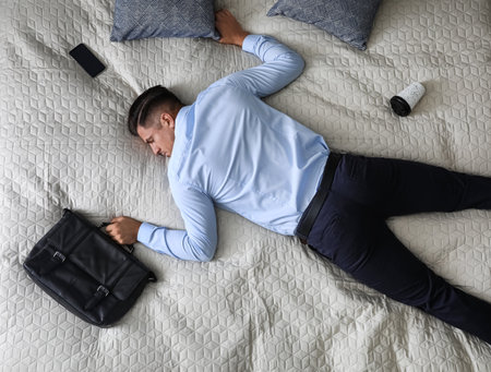Exhausted businessman in office wear sleeping on bed at home after work, above viewの写真素材