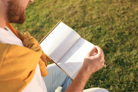 Young man reading book outdoors on sunny day, closeupの写真素材