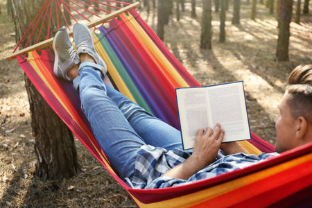 Man with book relaxing in hammock outdoors on summer dayの写真素材