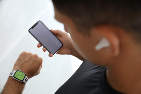 Man with smartphone checking fitness tracker in gym, closeup