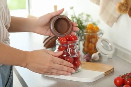 Woman pickling glass jar of tomatoes at counter in kitchen, closeupの写真素材
