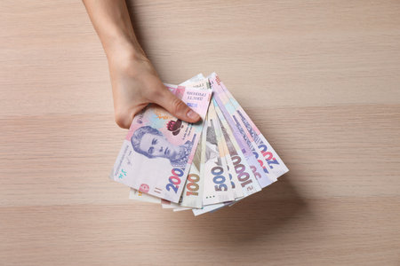 Woman holding Ukrainian money on wooden background, closeupの写真素材