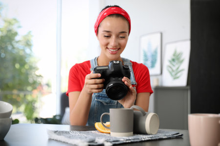 Young photographer taking picture of cups at table indoors, focus on cameraの写真素材