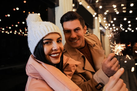 Couple in warm clothes holding burning sparklers near buildingの写真素材