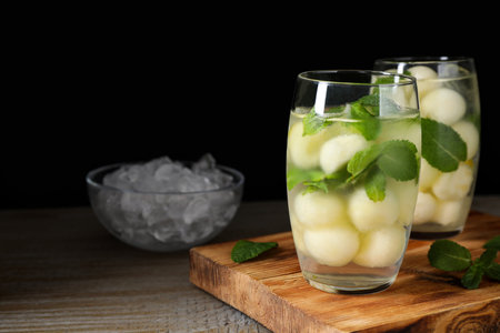 Tasty melon ball drink on wooden table against black background. Space for textの写真素材