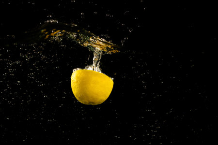 Lemon half falling down into clear water against black backgroundの写真素材