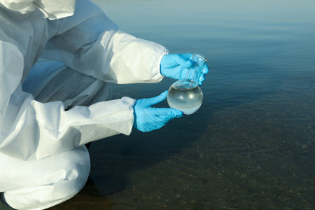 Scientist in chemical protective suit with florence flask taking sample from river for analysis, closeupの写真素材