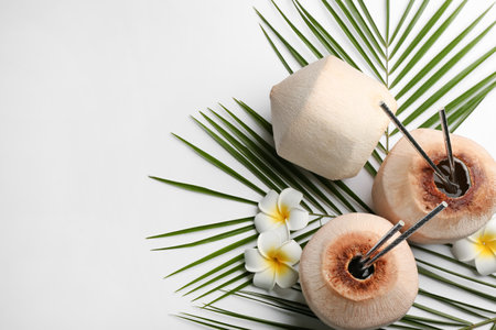 Fresh coconuts with drinking straws and flowers on white background, flat lay. Space for textの写真素材