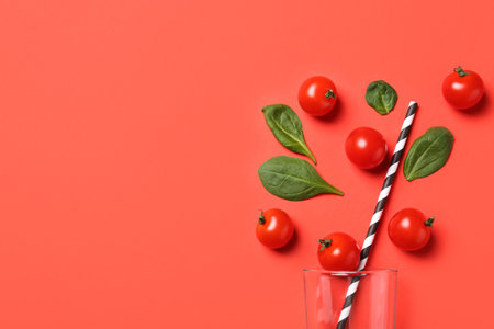 Cherry tomatoes, spinach leaves and glass with straw on coral background, flat lay. Space for textの写真素材