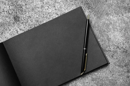 Open sketchbook with black pages and pen on gray stone table, top viewの写真素材