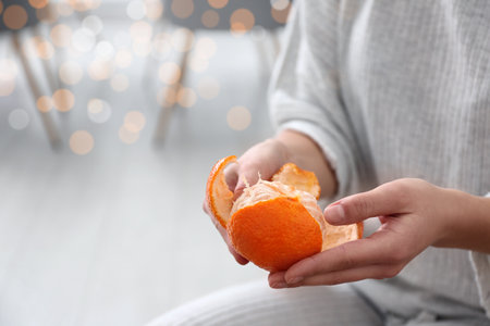 Woman peeling tangerine on blurred background, closeup. Space for textの写真素材