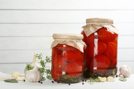 Glass jars of pickled tomatoes and ingredients on white wooden tableの写真素材