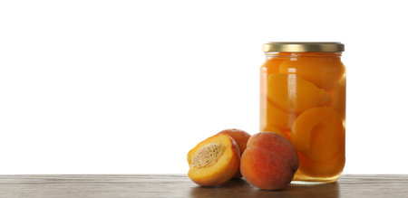 Glass jar of pickled peaches and fresh fruits on wooden table against white background. Space for textの写真素材
