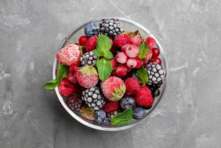 Mix of different frozen berries in bowl on grey table, top viewの写真素材