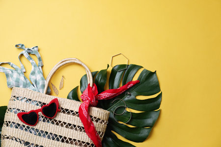 Stylish straw bag and summer accessories on yellow background, flat lay. Space for textの写真素材