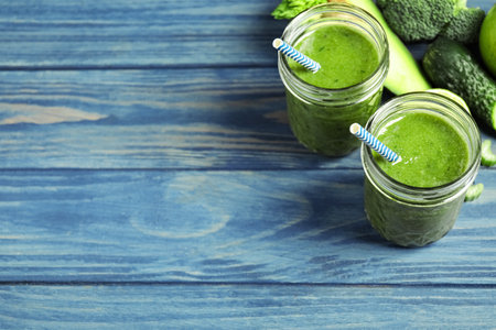 Delicious green juice and fresh ingredients on blue wooden table, space for textの写真素材