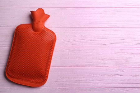 Hot water bottle on pink wooden background, top view. Space for textの写真素材
