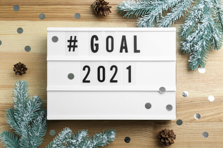 Light box with hashtag Goal 2021 near fir branches and cones on wooden table, flat lay. New year targetsの写真素材