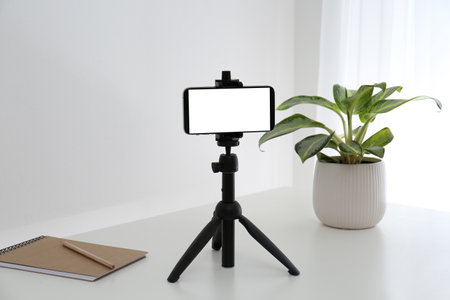 Smartphone with blank screen fixed to tripod on white table indoors. Mockup for designの写真素材