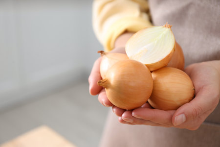 Woman holding golden onions indoors, closeup. Space for textの写真素材