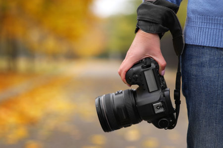 Photographer with professional camera outdoors on autumn day, closeup. Space for textの写真素材