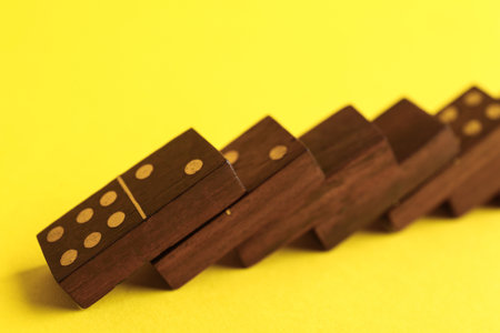 Falling wooden domino tiles on yellow background, closeupの写真素材