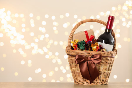 Wicker basket with gifts, wine and food against blurred festive lights. Space for textの写真素材