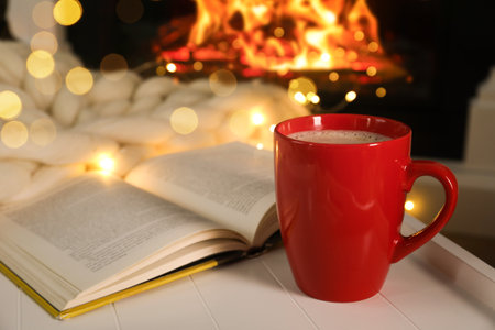 Cup of hot drink and book near fireplace. Cozy Christmas atmosphereの写真素材