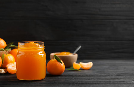 Tasty tangerine jam in glass jar on dark wooden table. Space for textの写真素材